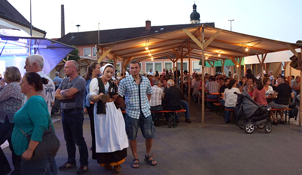 Feiernde unter einem Zeltdach, eine historisch gekleidete Kellnerin mit Bier im Vordergrund