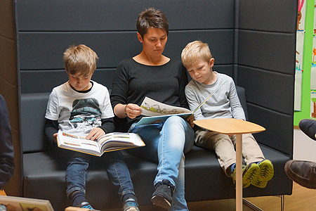 Mutter mit zwei Kindern in einer Leseecke sitzend