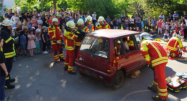 Feuerwehrleute öffnen ein Auto mit simulierten Verletzten, umringt von Schülerinnen und Schülern